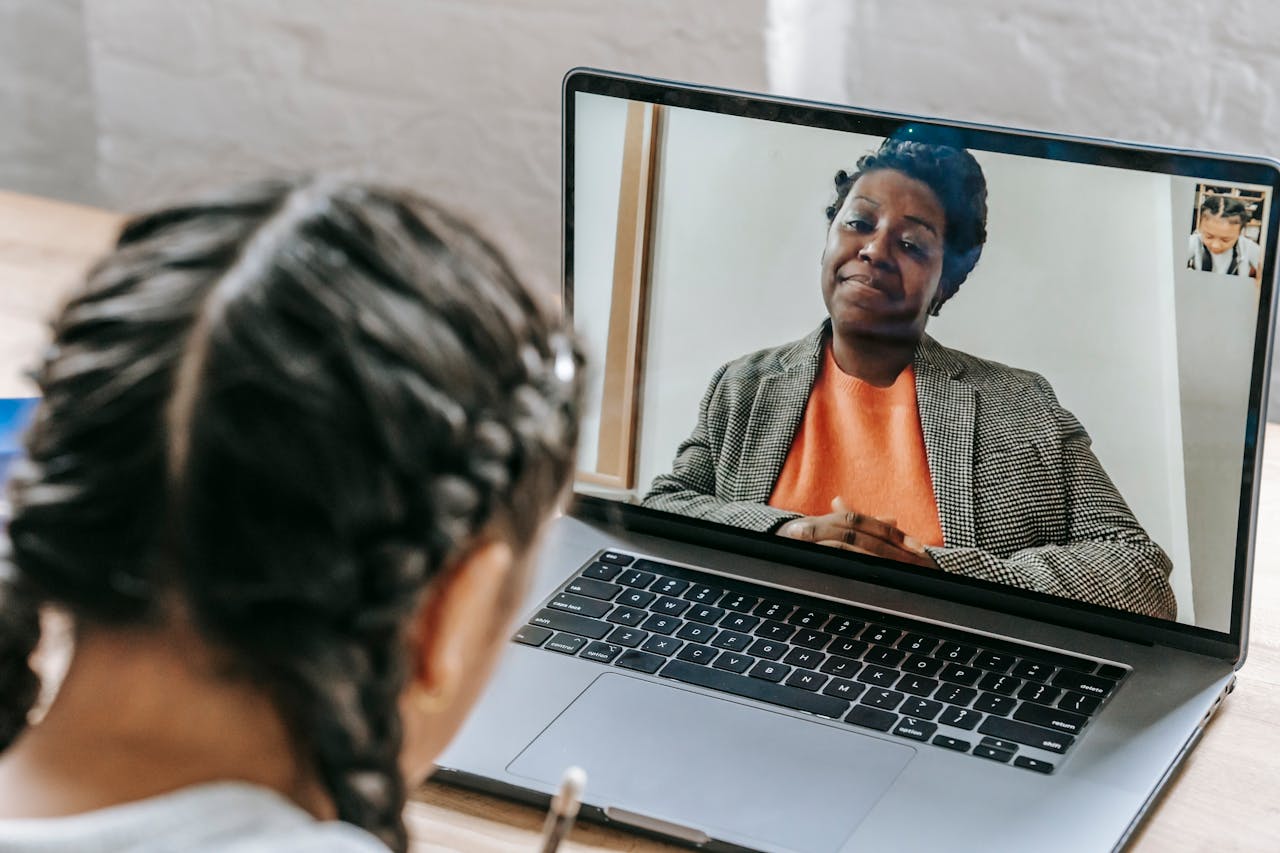 Child using laptop for online learning with teacher on video call, enhancing education at home.