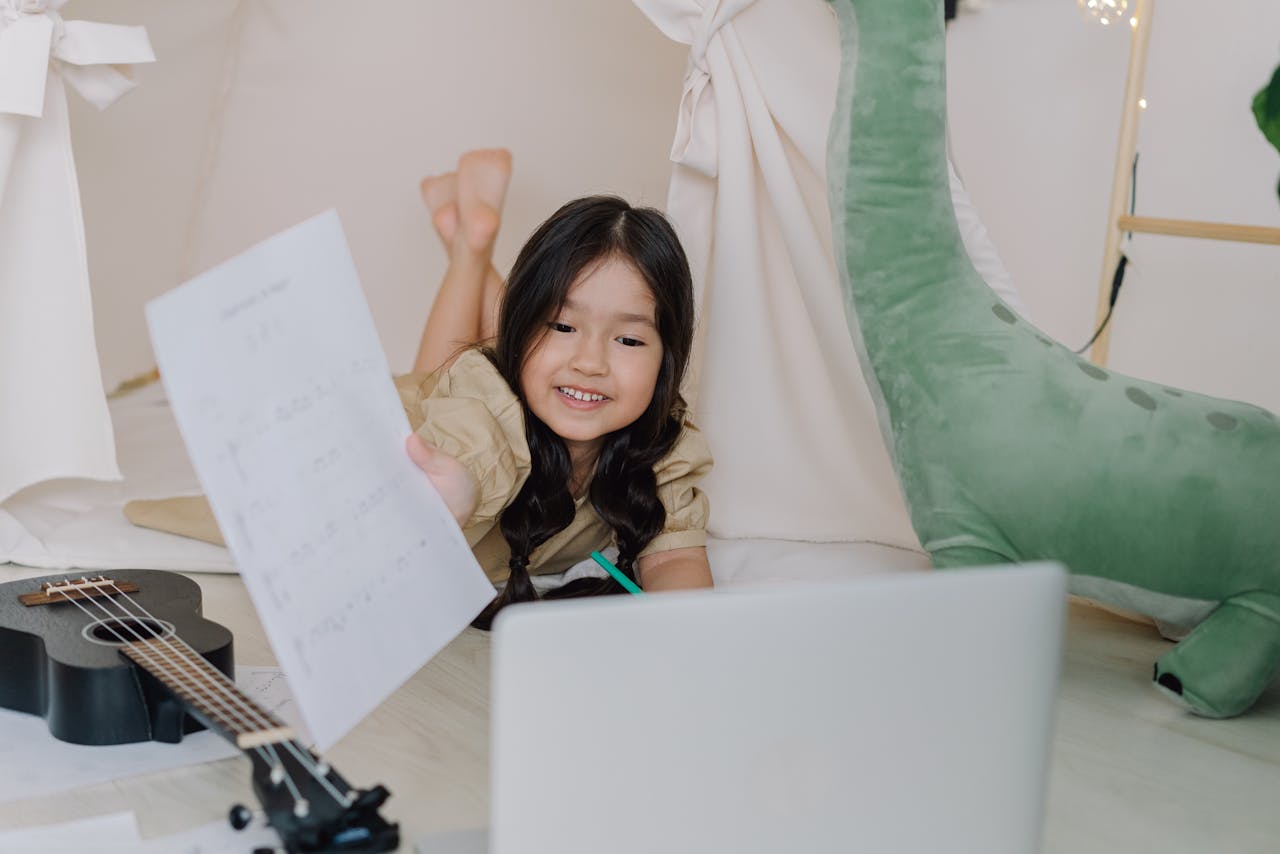 services-01 Happy child learning ukulele online at home with sheets and laptop, showing engaging childhood education.